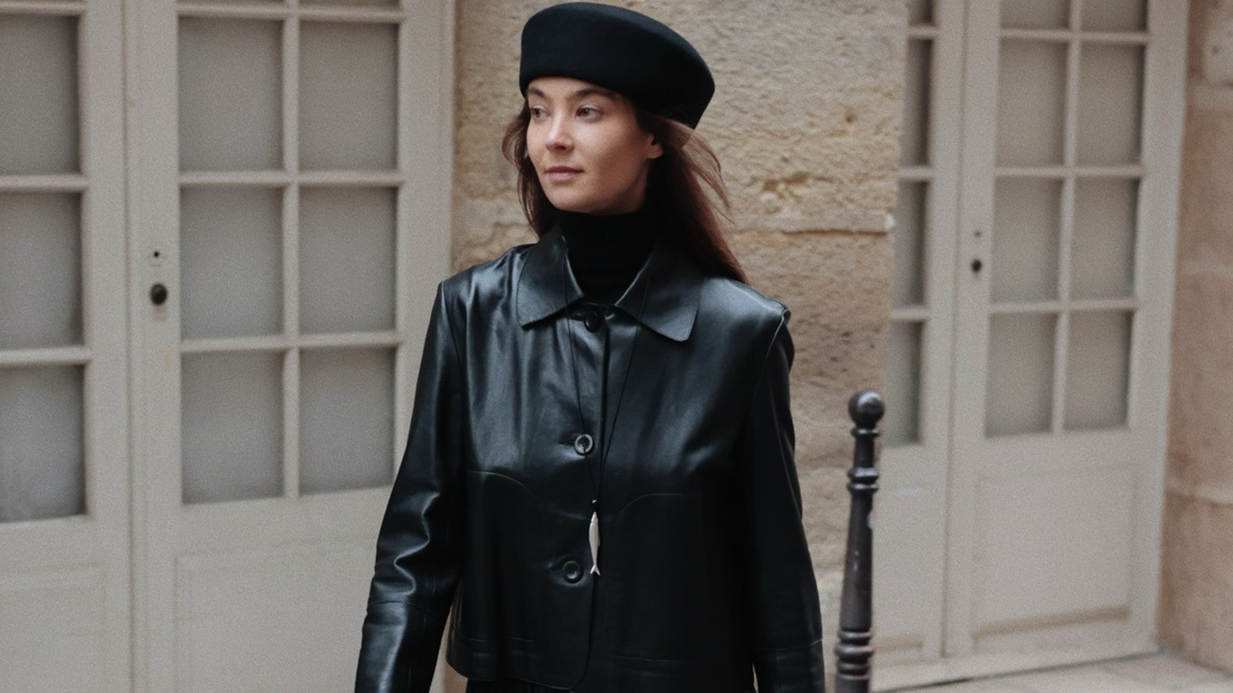 Woman wearing black leather jacket, black pillbox hat, and black gloves.