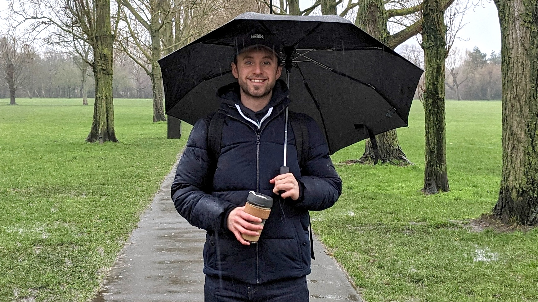 James Frew holding an umbrella on a walk in the rain with a KeepCup in his hand