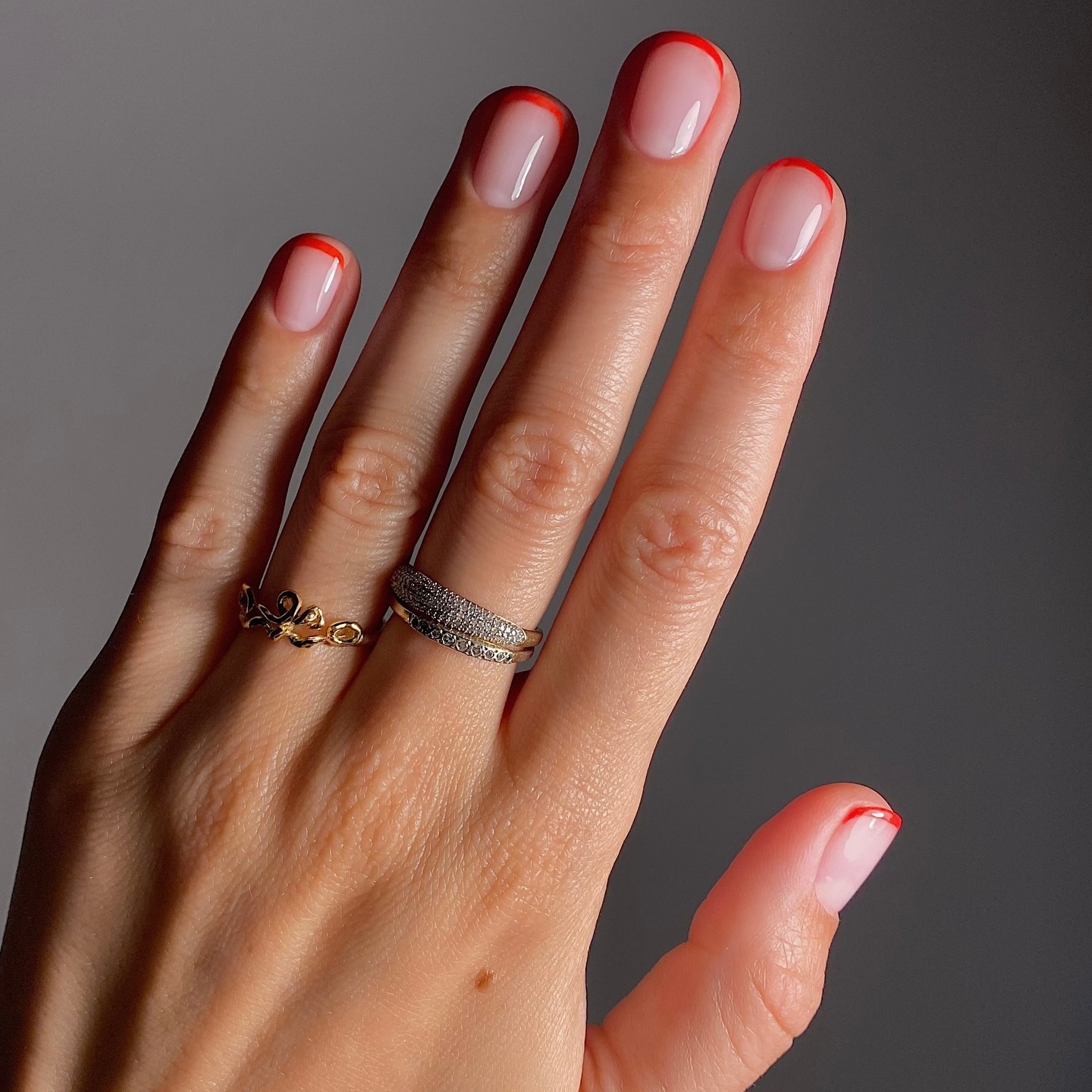 Photo of a red French manicure in front of a gray wall 