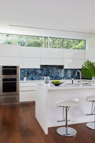 kitchen with white cabinets and white bar stools and high windows and blue crystal back splash