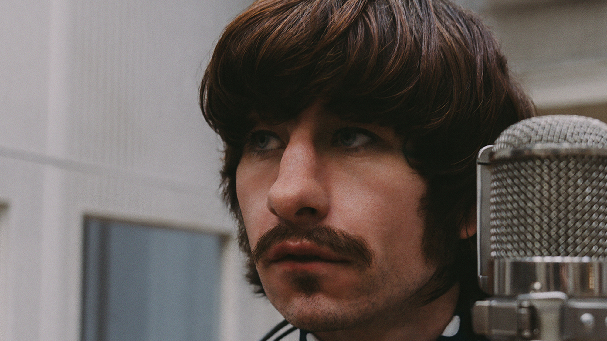 Barry Keoghan as Ringo Starr with a mustache, in cliseup, with a microphone next to him.