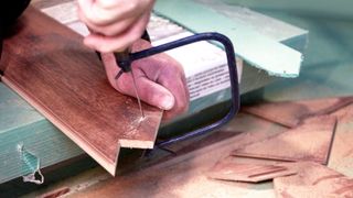 Hand using a coping saw to cut dark wood flooring plank