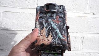 Browning Strike Force HD Pro X trail camera held in hand in front of white bricks