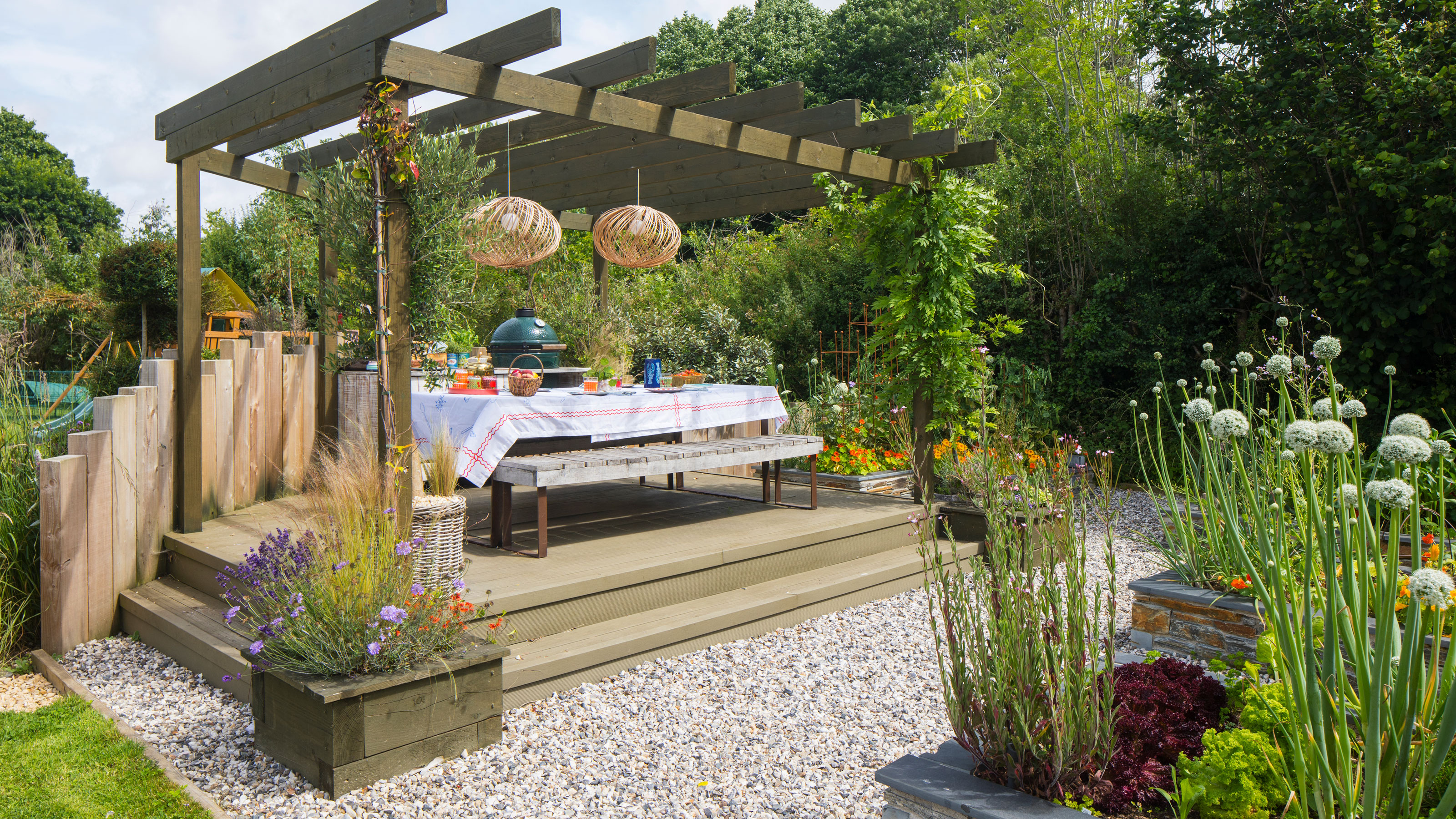 Garden with wooden pergola over wooden deck and lights having over the dining table.