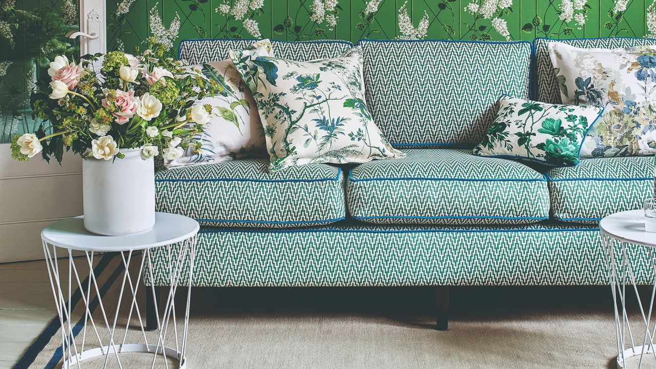 A living room with a green floral wallpaper with a patterned sofa in front of it with contrasting blue piping