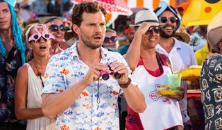 Barb and Star Go to Vista Del Mar Jamie Dornan stands shocked holding a small pair of binoculars