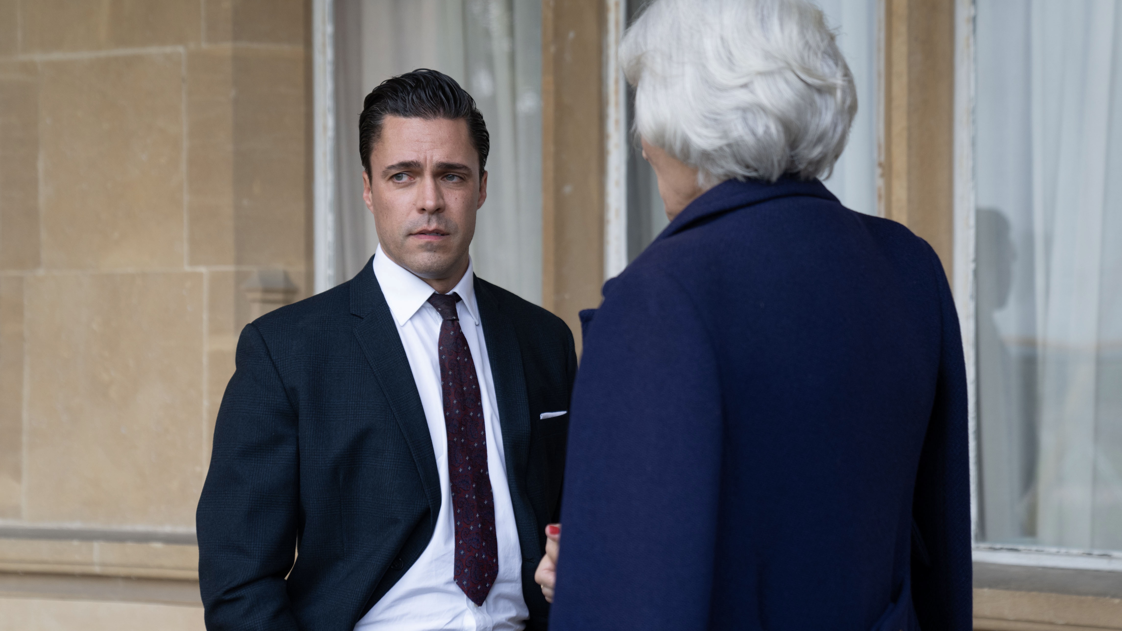 Olly Rix in a dark suit as Matthew talks to Terry Bamberger in a dark jacket as Lady Aylward in Call the Midwife