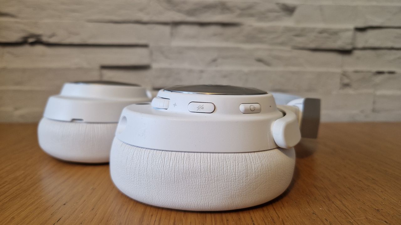 The SteelSeries Arctis Nova Pro Wireless white edition on a wooden surface with a white brick background
