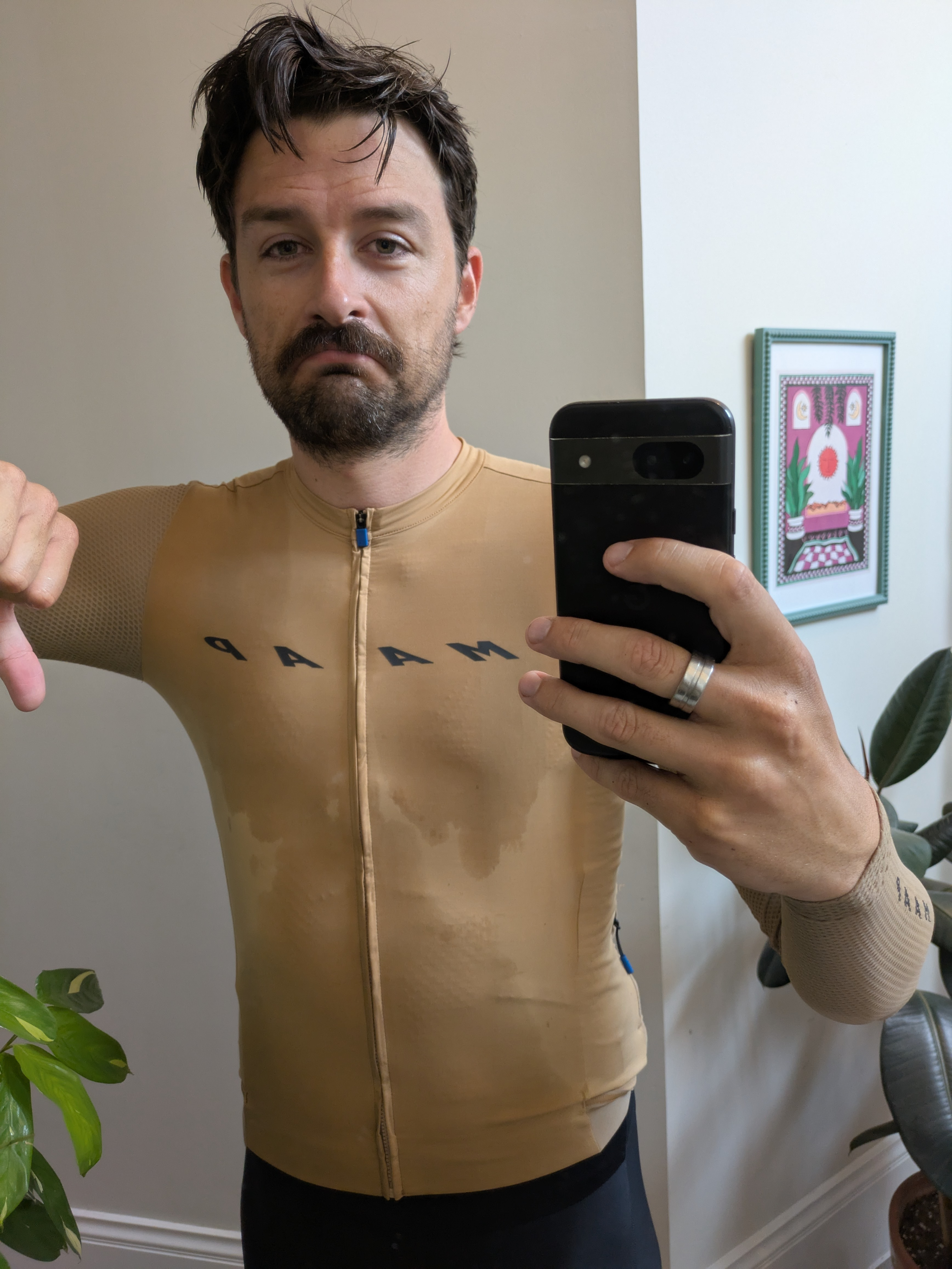 A man in a beige cycling jersey, visibly wet, gives a thumbs down