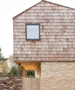 exterior of home with timber shingles on top section, pale brick on lower half, dark brick wall and timber cladding on overhang walkway