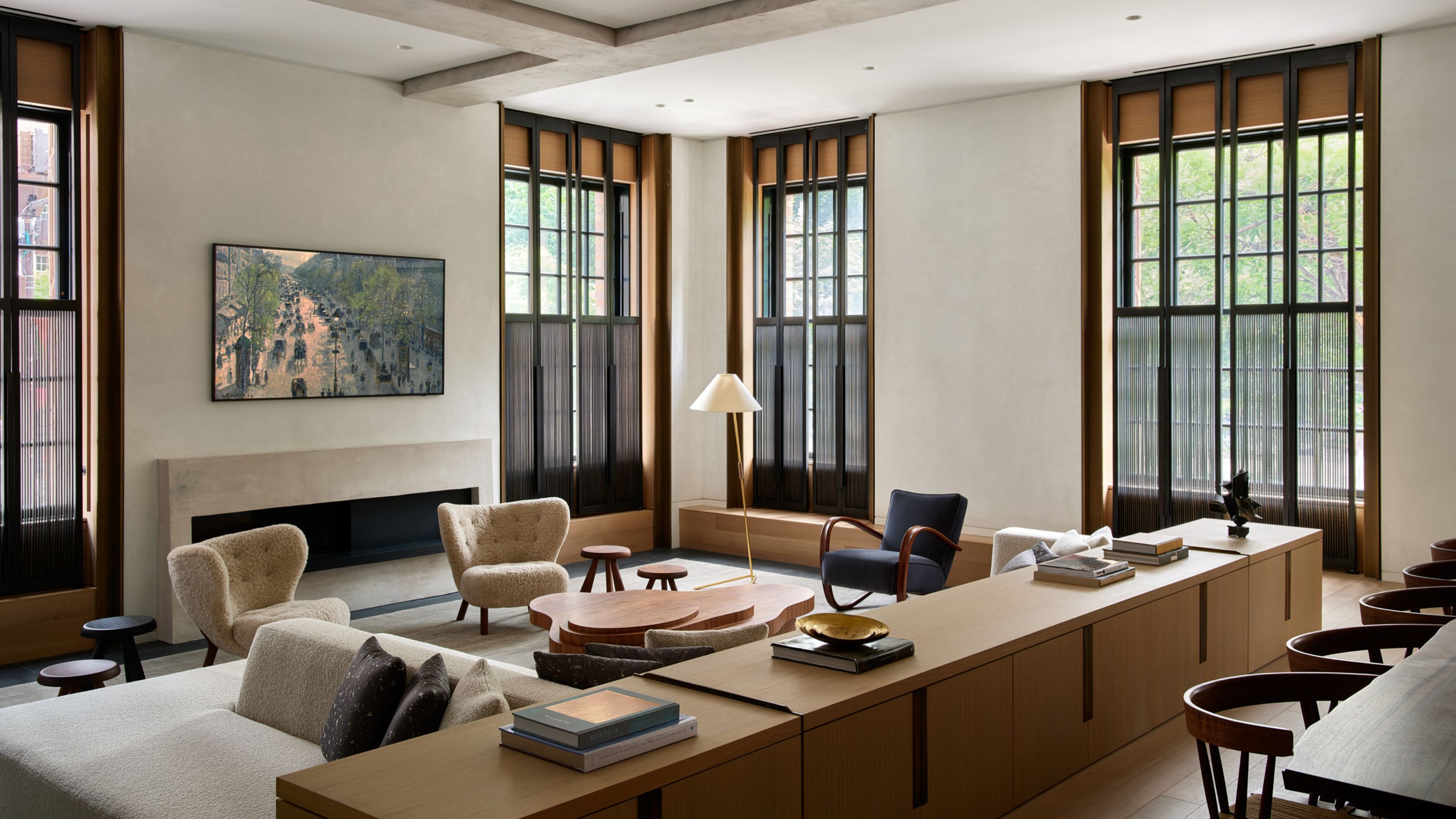 Neutral living room with large windows, a low stone fireplace, boucle armchairs, long wooden console to divide the space from the dining area