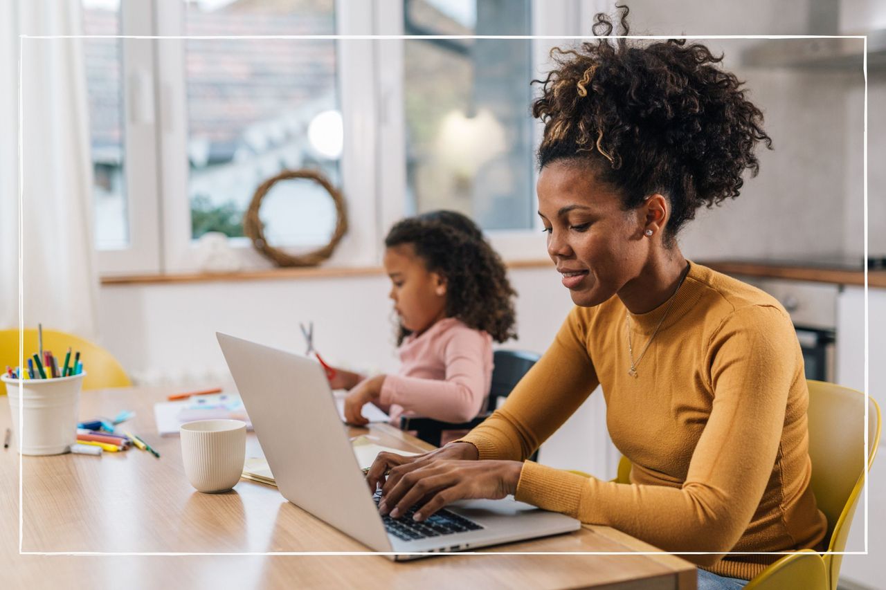 Mum working on laptop at home with daughter sitting beside her at the table