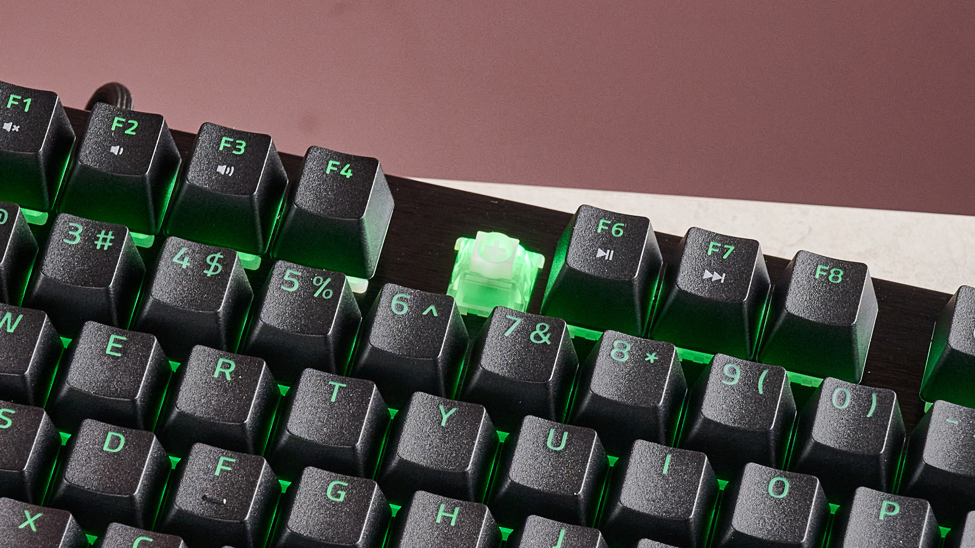 Close-up of top row of keys on Razer Huntsman V3 HE Magnetic Tenkeyless 8KHz with F5 keycap removed, on a desk with pink wall in background