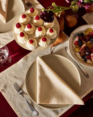 Christmas table setting with a red table cloth, white placemats, and white plates and napkins. There is a plate of raspberry sweets set up in the center of the table