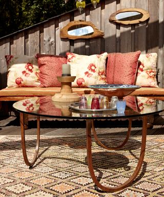 Rustic roof garden ideas example with wooden planks, red and cream cushions and a curved glass coffee table.
