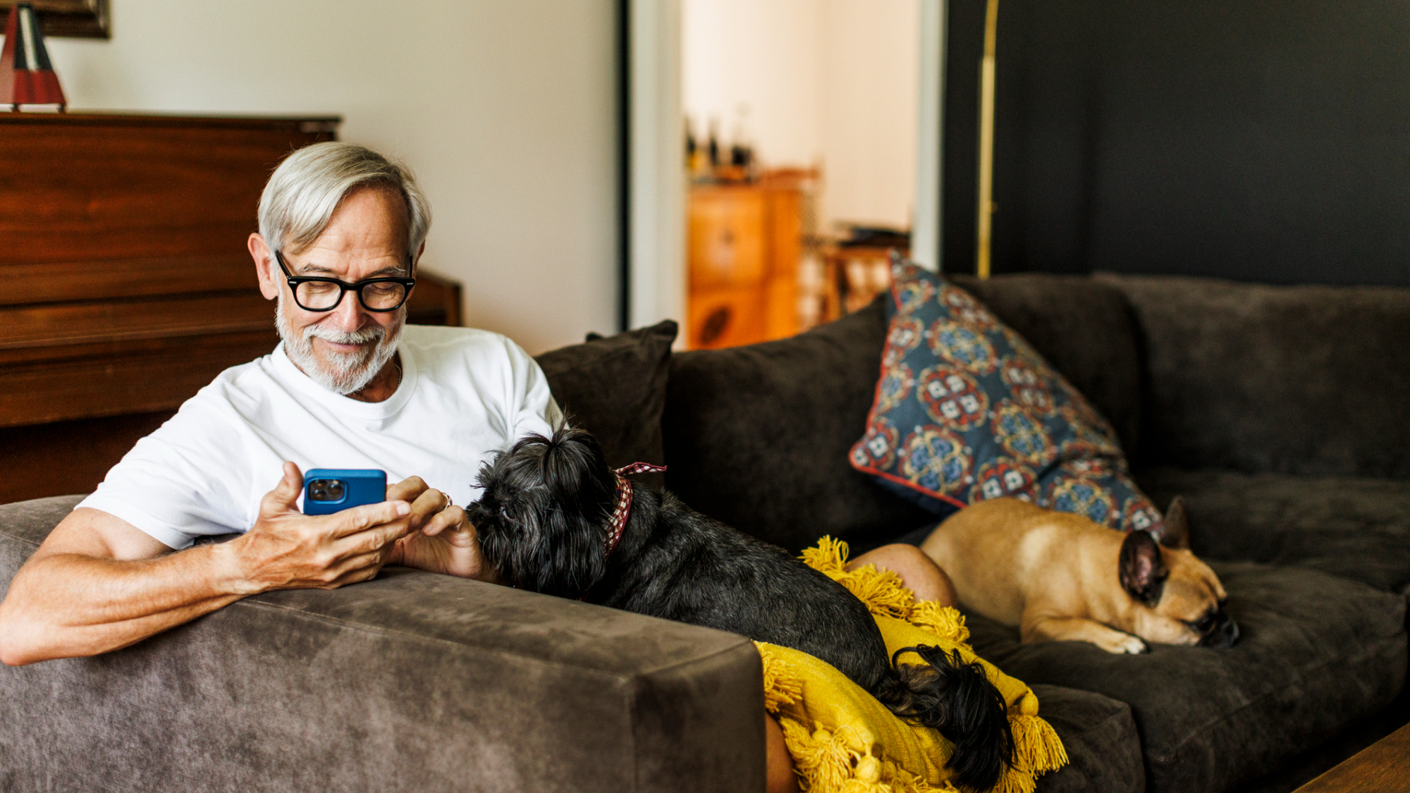 A person, sat on a sofa looking at their iPhone, with a dog.