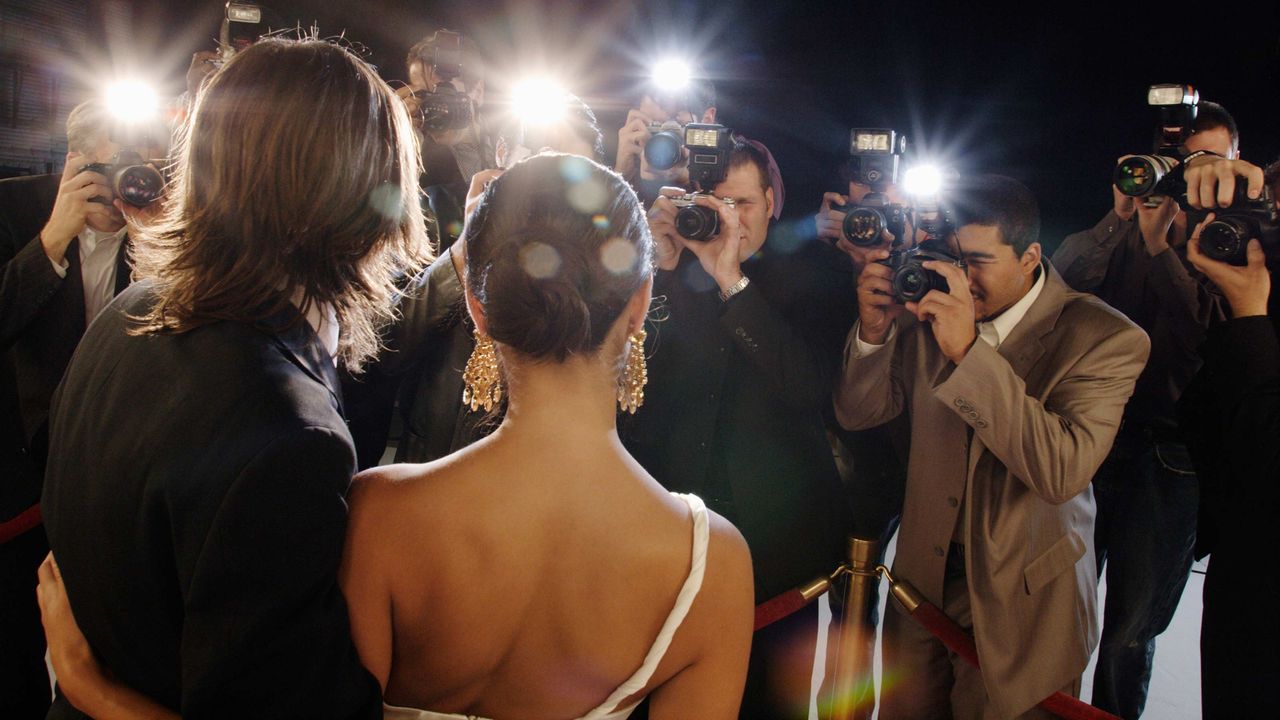 The paparazzi photograph a glamorous couple.