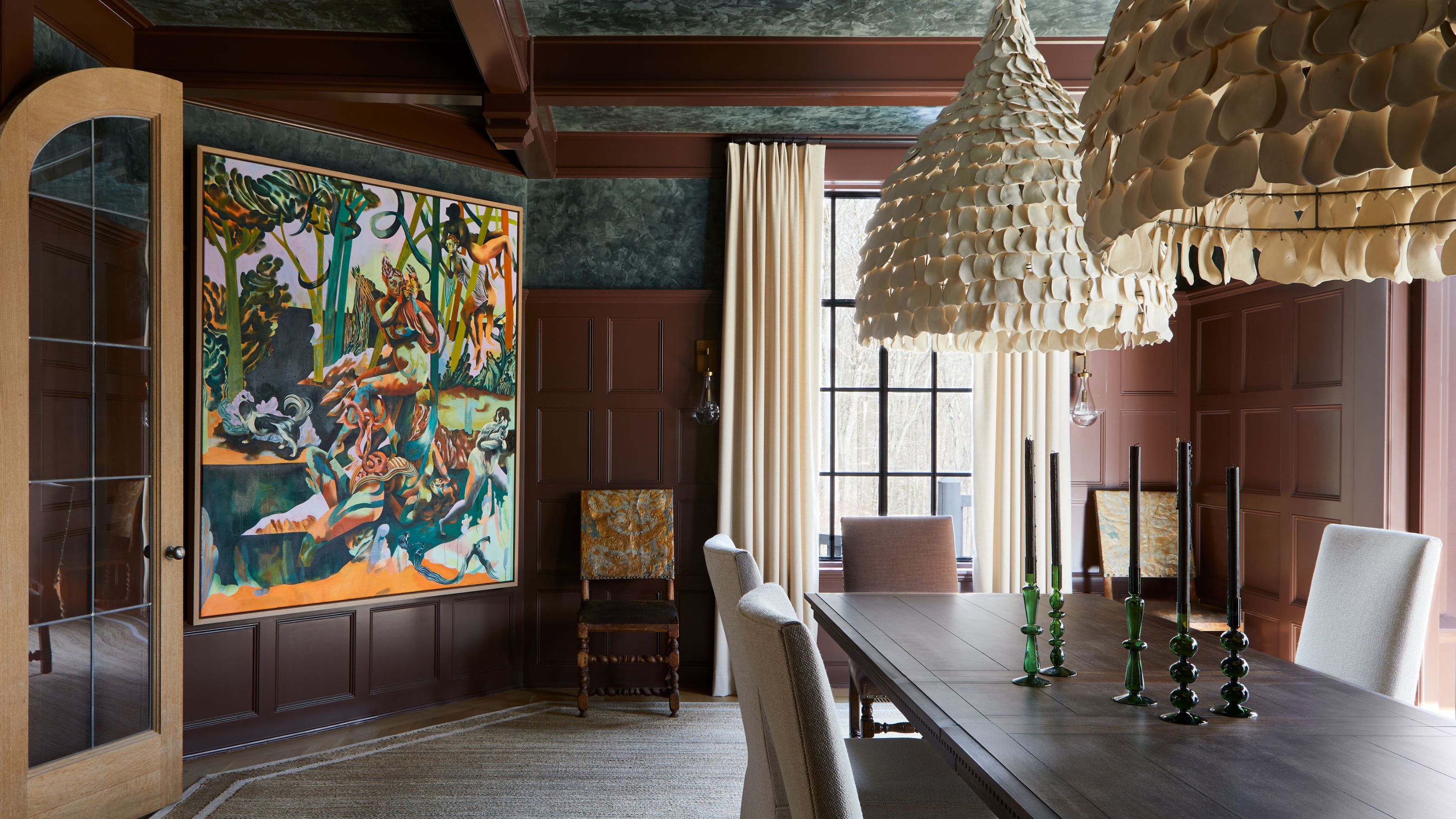A large formal dining room with brown panelling, emerald green plaster on the ceiling and upper portion of the walls, a large dark wood dining table, an abstract artwork, and modern cream pendant lights.