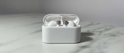 White and silver 1More PistonBuds Pro Q30 earbuds sitting in the charging case with the lid open. The case is sitting on a white marble-effect desk.