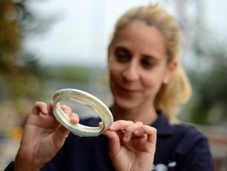 Archaeologist Limor Talmi of the Israel Antiquities Authority holds the base of a large glass bowl that was found in the same refuse pile as the fragment of glass bracelet.