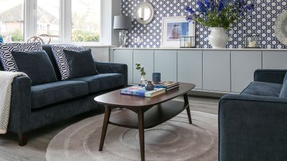 A pair of blue sofas arranged around a coffee table in a living room with white and blue circular patterned wallpaper.