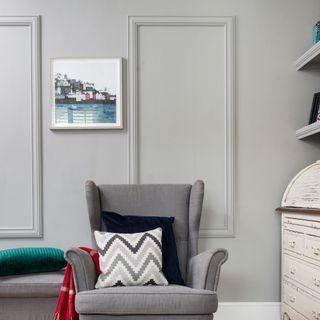 grey living room with a grey chair with a black and patterned pillow next to a white chest drawer