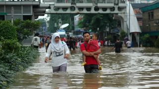 A couple with a baby walk through a street flooded with water past their knees