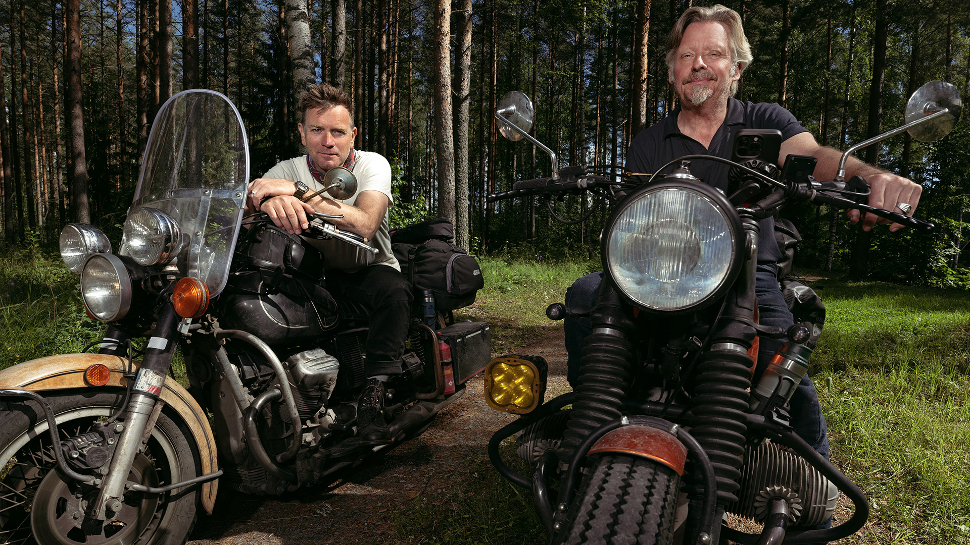 Two men sit on bikes in a forest