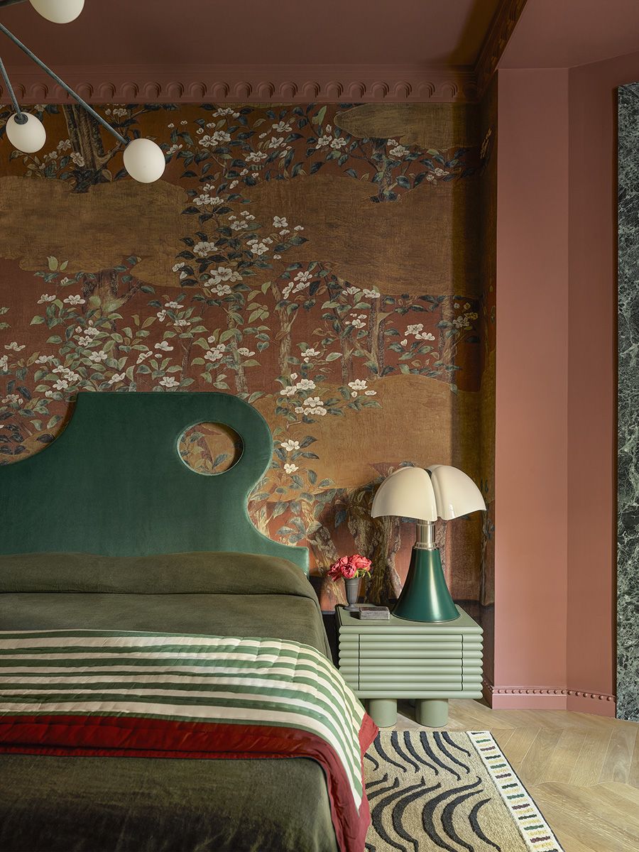 A contemporary bedroom featuring sculptural velvet bedframe, floral botanical wallpaper and sculptural lighting