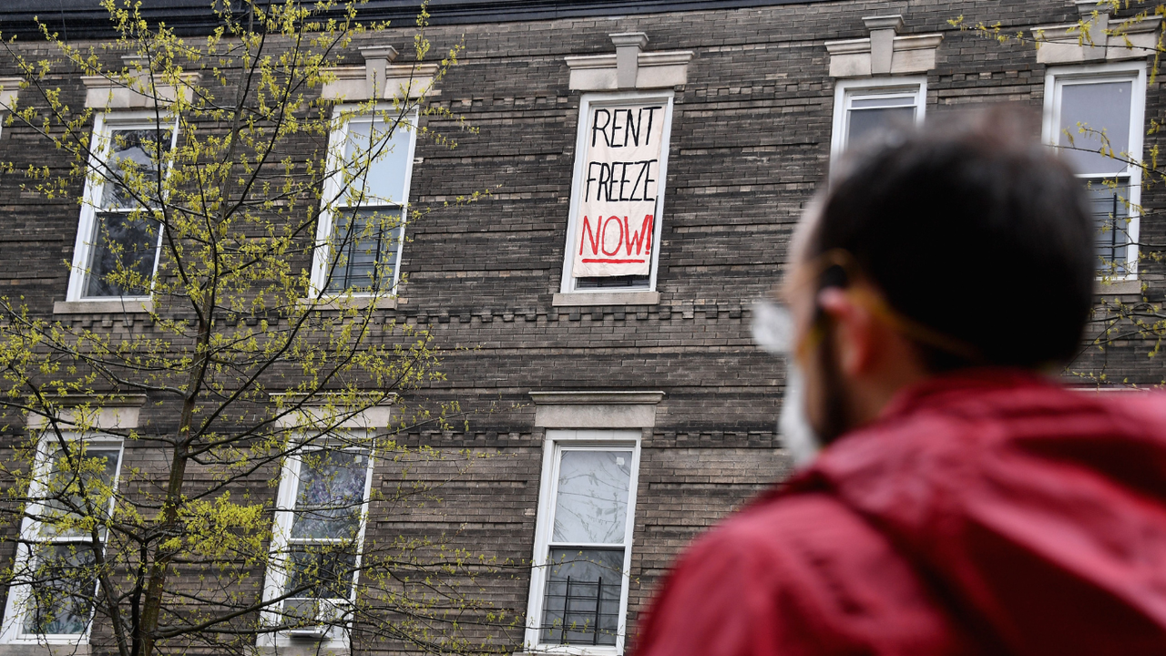 A man looks up at a window with a banner reading &amp;quot;Rent freeze now&amp;quot;