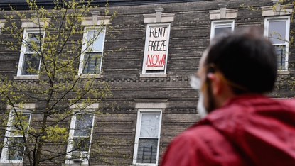 A man looks up at a window with a banner reading "Rent freeze now"