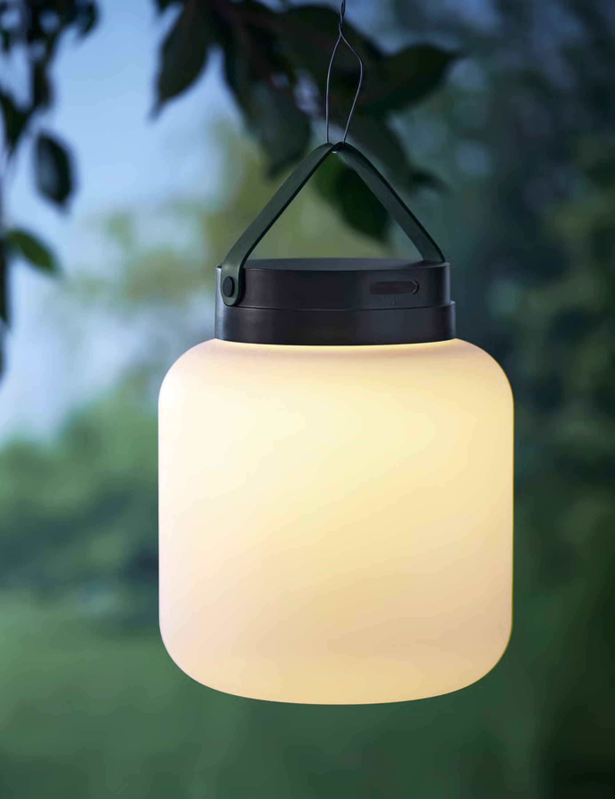 IKEA L&amp;Auml;NSPORT lamp softly aglow, hanging from a leafy tree branch.