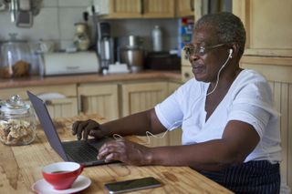 Older woman woman sitting at kitchen table using laptop