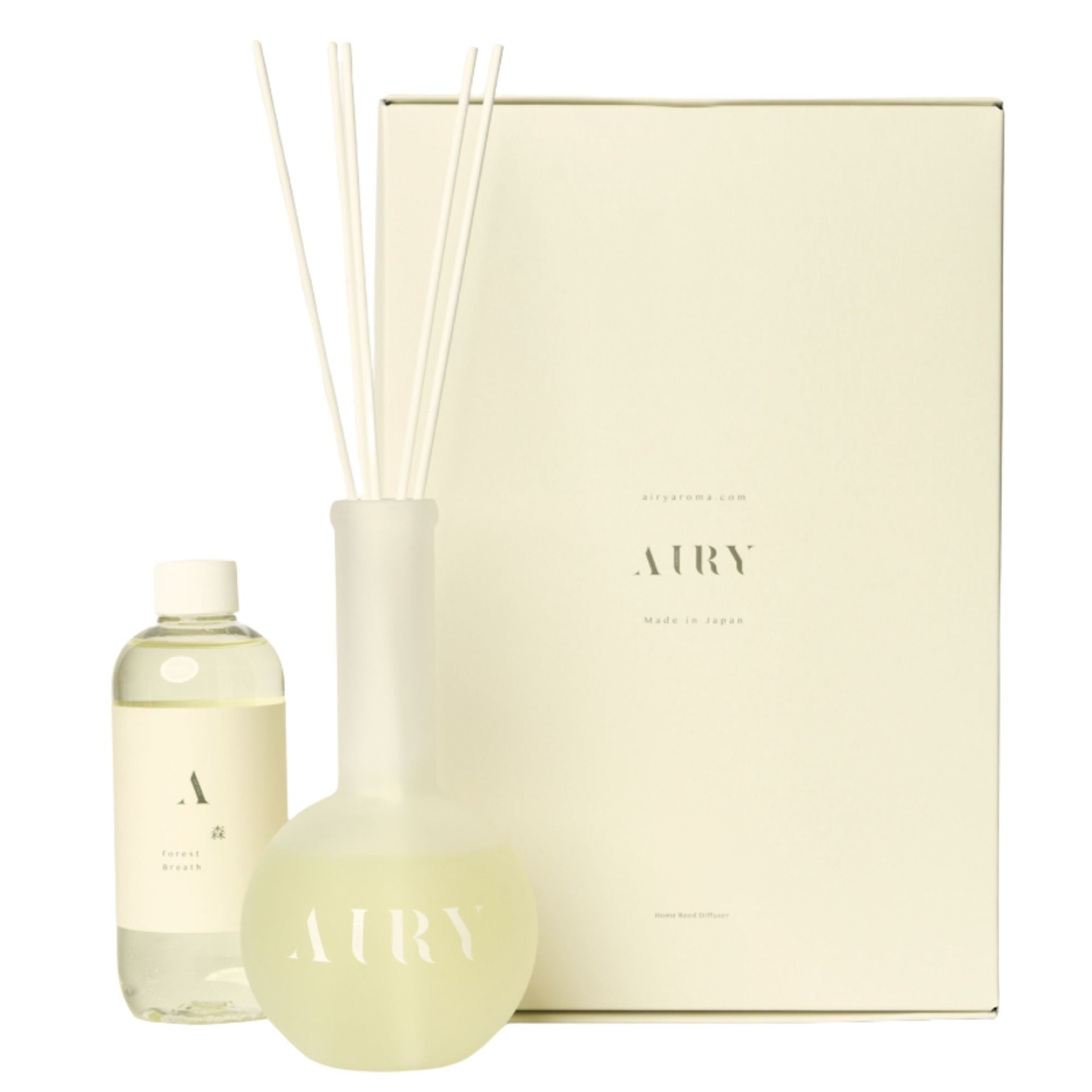 A glass Airy Fragrances reed diffuser filled with white reeds, with a clear bottle of refillable fragrance with a white lid, and a large cardboard packaging box