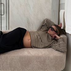 Sofia Richie Grainge lies on a sofa wearing a black and white striped knit with track pants and black sunglasses.