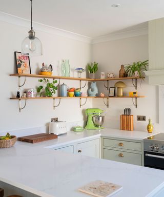 small pale green kitchen with corner shelving and white countertops