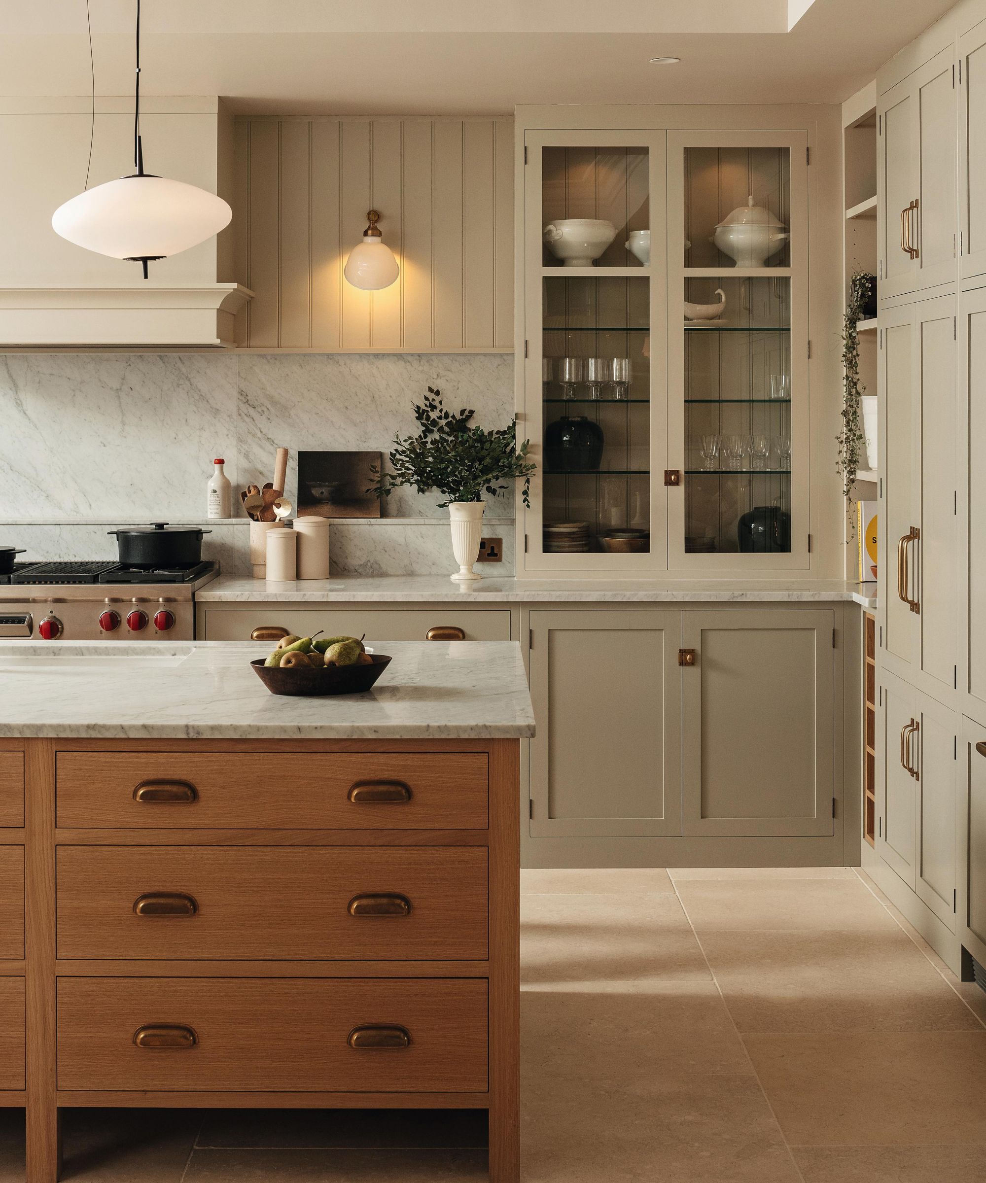 a warm neutral two tone kitchen with a glass fronted cabinet and a warm wooden island