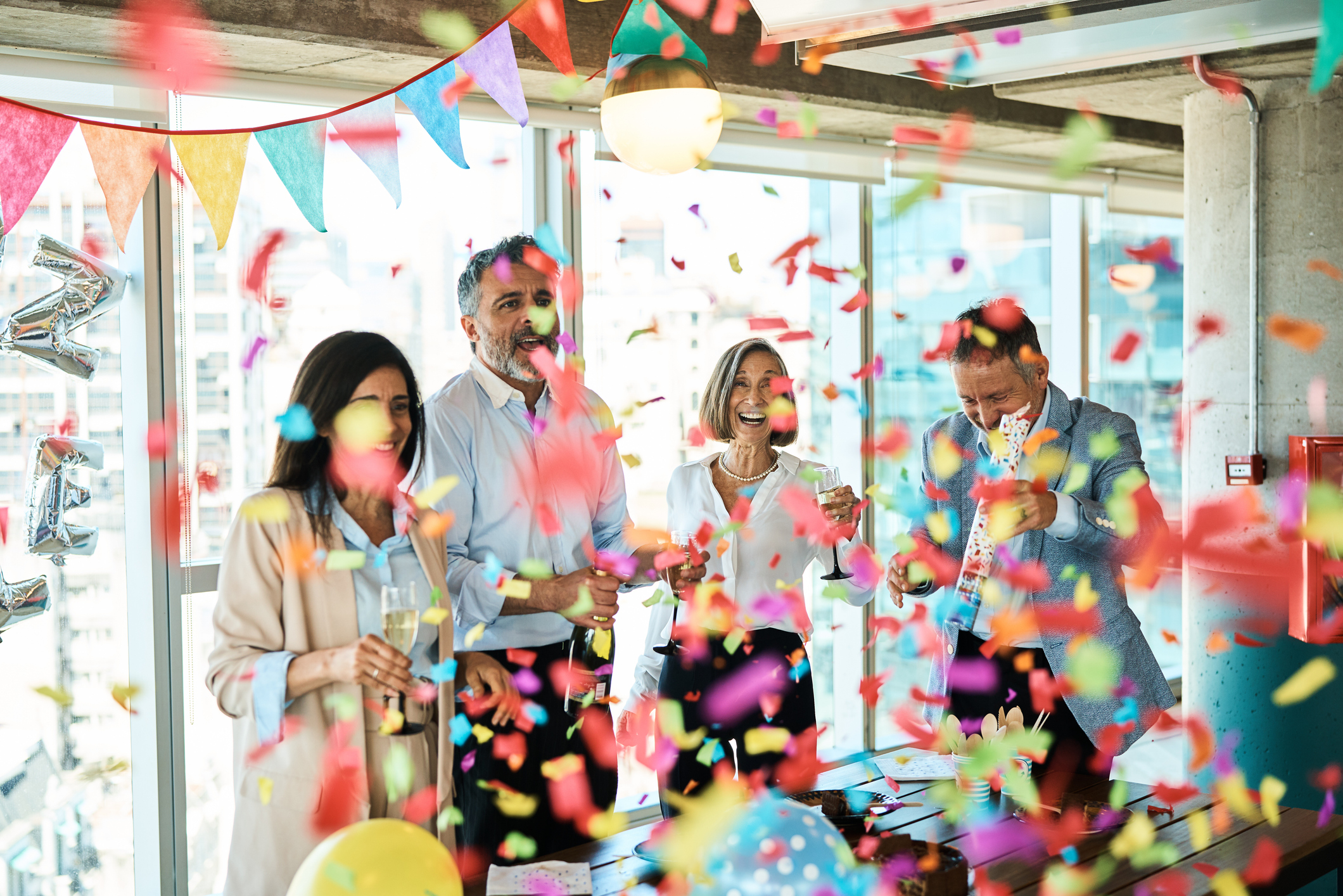 Mature business people celebrating birthday with confetti party popper in office. Group of male and female professionals celebrating birthday party in office.