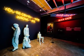 White mannequins in various poses in front of a wall with the words "YOU'RE OBVIOUSLY IN THE WRONG PLACE", and a red neon sign with the words "BLACK DAZE"