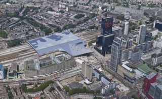Daytime, aerial view of Rotterdam Central Station, surrounding city landscape, buildings, roads, trees, cars, houses, rail tracks