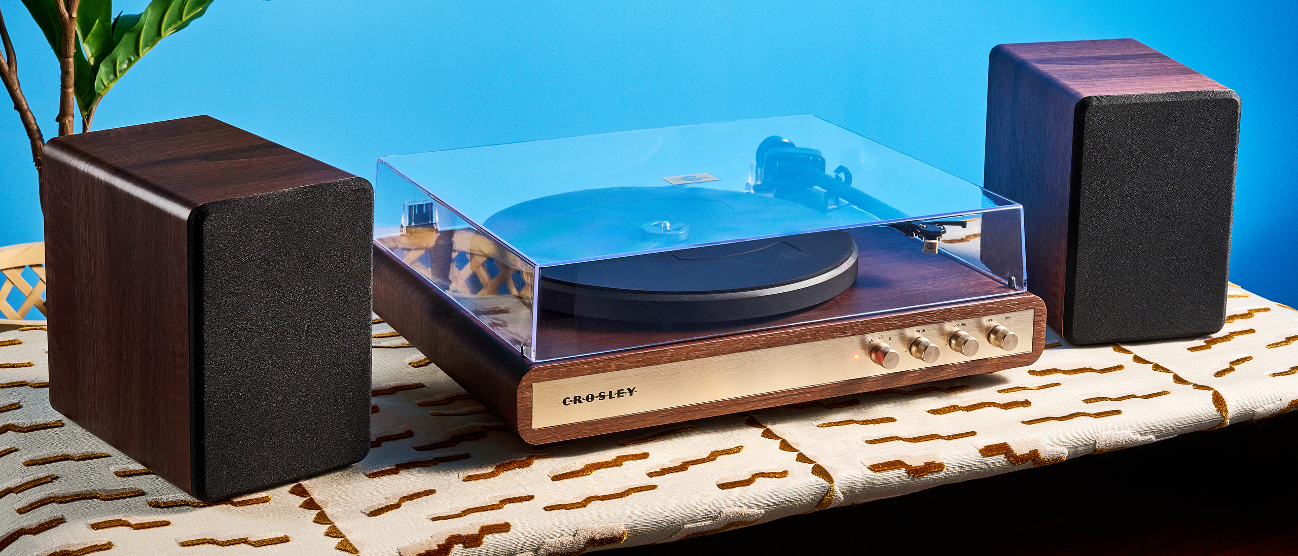 Crosley C65 turntable and bookshelf speakers photographed in front of a blue background on a brown table.