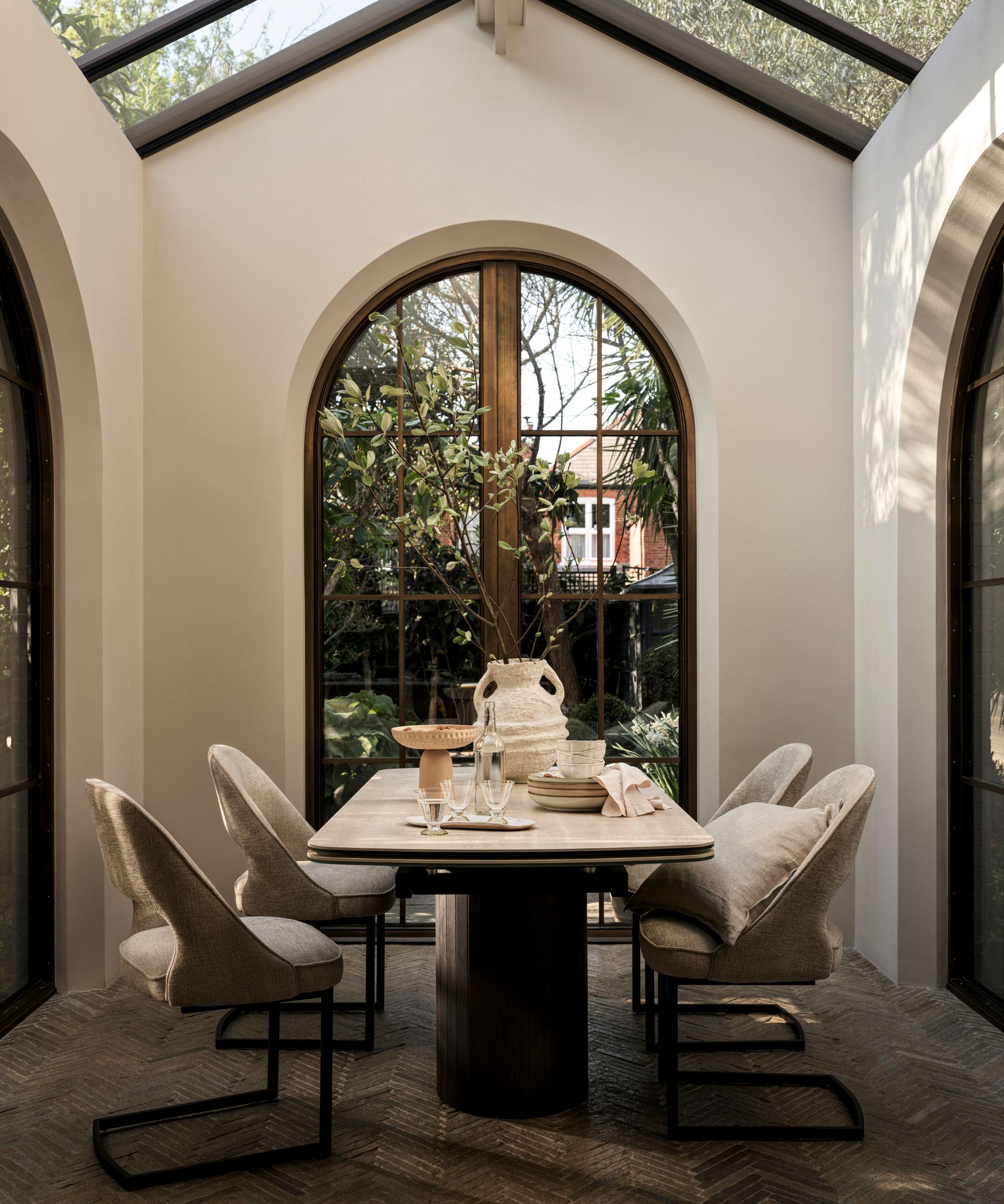 Pitched glass roof extension dining area with arched glass crittal doors on three sides with sleek minimalist dining table and upholstered chairs