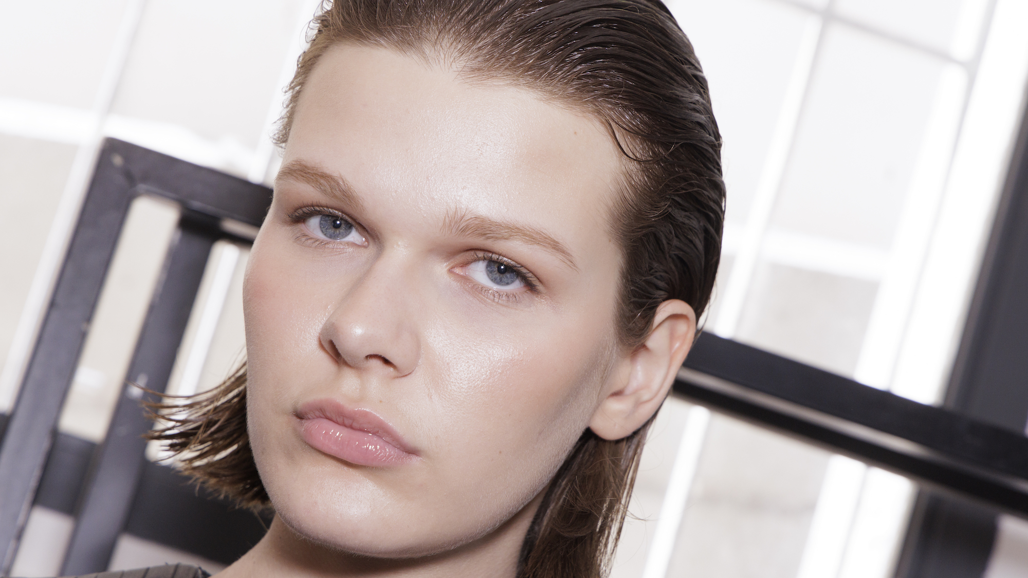 Model with bright dewy skin and slicked back hair backstage at fashion week
