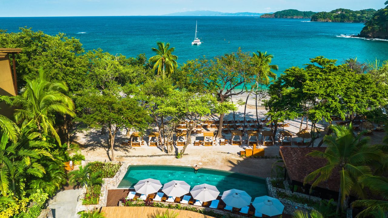 Overhead image of a pool area at a resort that connects to the beach and ocean.