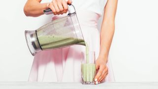 A woman tipping a green smoothie from a blender pitcher into a glass