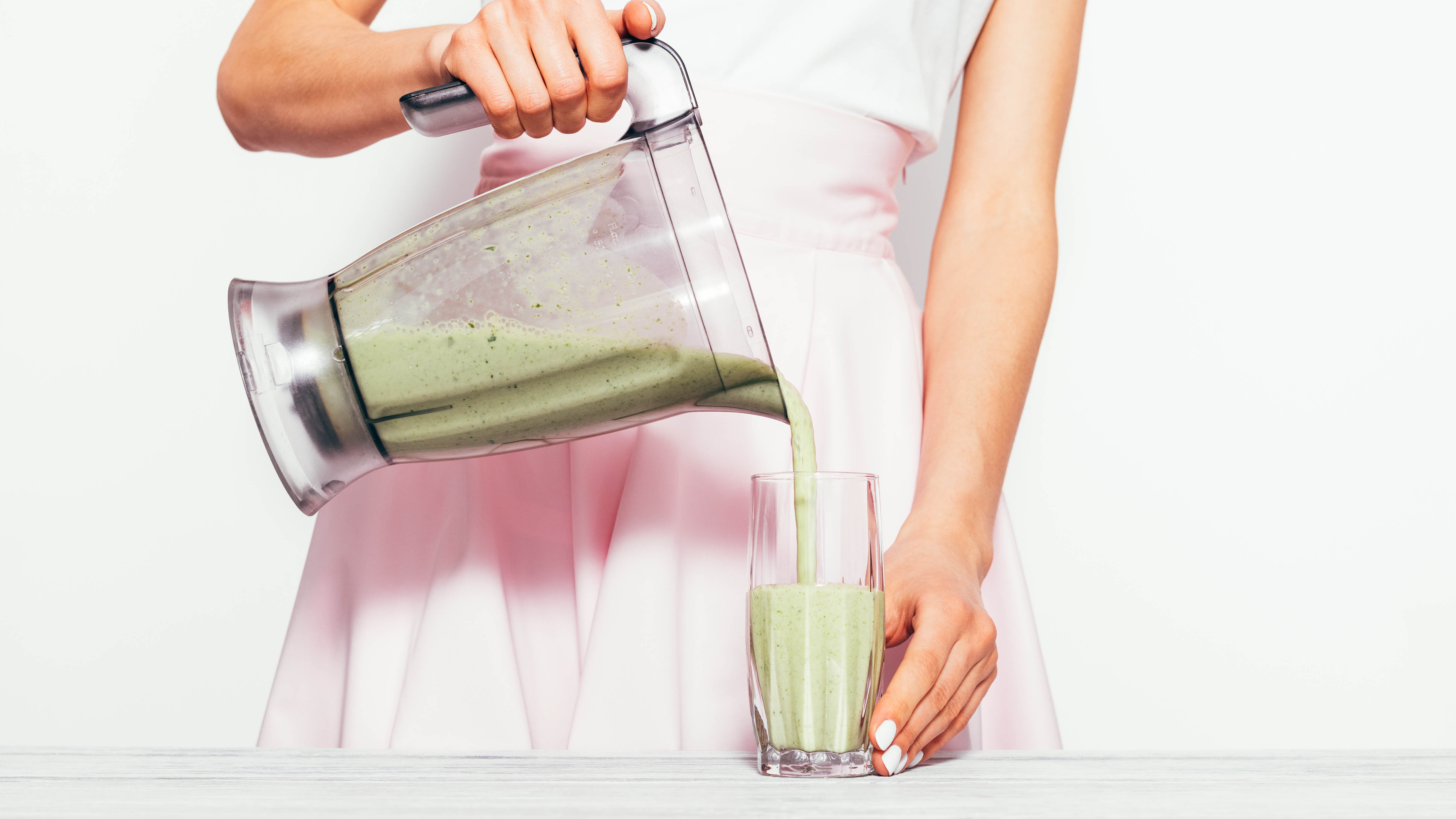 Женщина переливает зеленый смузи из кувшина блендера в стакан