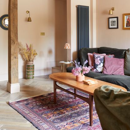 pale pink living room with black sofas with pink cushions, a wooden oval coffee table and persian rug underfoot