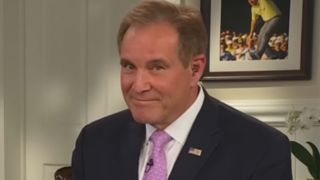 Jim Nantz smiling in a blue jacket and pink tie on a Masters broadcast. 