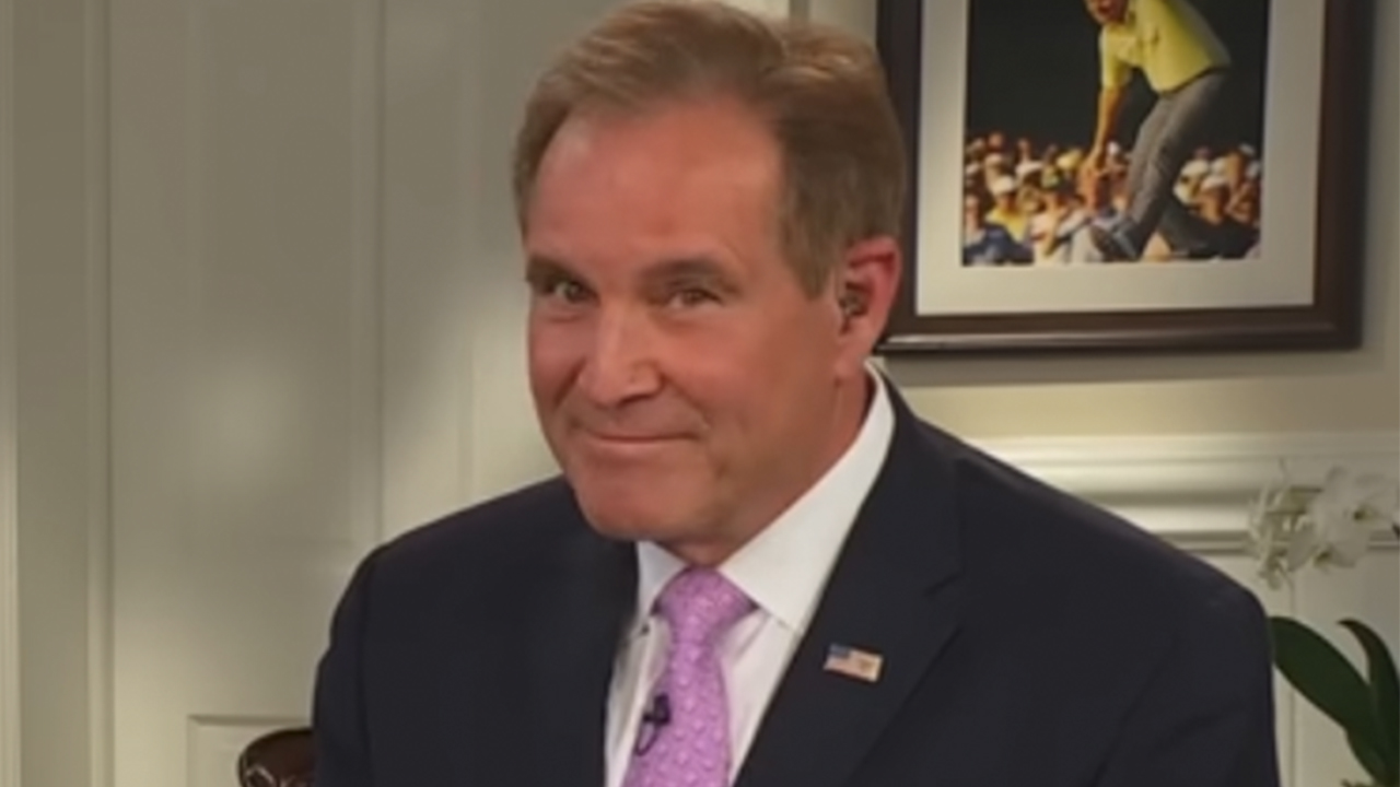 Jim Nantz smiling in a blue jacket and pink tie on a Masters broadcast.