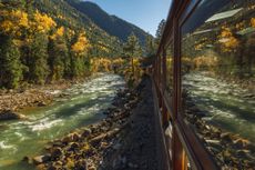 A river and a mountain scene reflect in the window of a passenger railroad car going through an autumn scene. Photo taken October 15 2022 near Durango Colorado, USA.